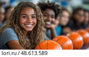 A group of young athletes, smiling and engaged, gather around basketballs during a team practice in a vibrant gymnasium. Стоковое AI-изображение, AI-художник Данила Большаков / Фотобанк Лори