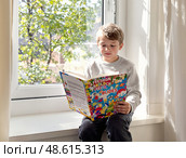 Ребёнок сидит у окна в классе, глубоко погружённый в чтение книги. На его лице отражается задумчивость и счастье. Яркие краски книги радуют глаз. Стоковое AI-изображение, AI-художник Сергей Никифоров-Гордеев / Фотобанк Лори