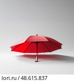 Bright red umbrella stands alone against a neutral background, showcasing its vibrant color and unique design in indoor light. Стоковое AI-изображение, AI-художник Сергей Толмачёв / Фотобанк Лори