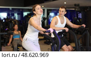 Determined young man and woman training with air-bike in fitness hall during full-body workout. Стоковое видео, видеограф Яков Филимонов / Фотобанк Лори