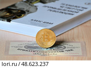 Приватизационный чек 1992 года и сувенирный биткоин на фоне книги о технологиях четвертой промышленной революции. Редакционное фото, фотограф Владимир Литвинов / Фотобанк Лори