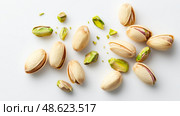 Healthy snack options include pistachios scattered on a white surface with some shells open and others closed. Стоковое AI-изображение, AI-художник Сергей Толмачёв / Фотобанк Лори