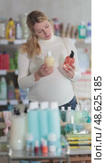 Thoughtful young expecting mother in household store examining two liquid soap bottles, comparing ingredients to find safest and gentlest option for family. Стоковое видео, видеограф Яков Филимонов / Фотобанк Лори