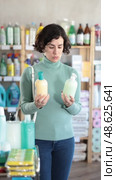 Pleased woman in her middle ages reviewing liquid hand soaps to buy at supermarket. Стоковое видео, видеограф Яков Филимонов / Фотобанк Лори