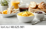Delicious breakfast spread featuring creamy scrambled eggs, toast, and various spreads on a stylish dining table. Стоковое AI-изображение, AI-художник Сергей Толмачёв / Фотобанк Лори