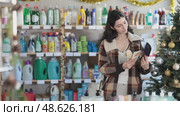 Happy young female buyer choosing convenient comb in large shop with New Year decoration. Стоковое видео, видеограф Яков Филимонов / Фотобанк Лори