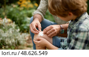Care and attention in a garden as a parent tends to a child's scraped knee on a sunny day. Стоковое AI-изображение, AI-художник Сергей Толмачёв / Фотобанк Лори