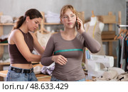 Young tailoress measuring female client speaking on mobile. Стоковое фото, фотограф Яков Филимонов / Фотобанк Лори