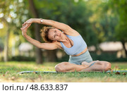 Woman practicing hatha yoga in garden, stretching in an asymmetrical seated asana Parivritta Janu Sirsasana. Стоковое фото, фотограф Яков Филимонов / Фотобанк Лори