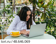 Young woman works with laptop on terrace of  cafe. Hunched posture, professional spinal deformity concept. Стоковое фото, фотограф Алена Аксенова / Фотобанк Лори