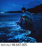 Seated on the sandy shoreline, an individual observes the mesmerizing blue glow of bioluminescent waves at night while the sky sparkles with stars. Стоковое AI-изображение, AI-художник Данила Большаков / Фотобанк Лори