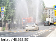 A water spraying vehicle refreshes the asphalt on a busy street while cars pass by in the summer heat, providing relief to pedestrians (2024 год). Редакционное фото, фотограф Данила Большаков / Фотобанк Лори