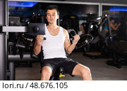 Slender athletic man work out muscles of arms and shoulders on simulator in gym of fitness club. Стоковое фото, фотограф Яков Филимонов / Фотобанк Лори