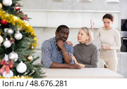 Old woman trying to calm angry man while middle-aged woman quarreling to him in the kitchen with Xmas-tree. Стоковое фото, фотограф Яков Филимонов / Фотобанк Лори