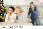 Man on christmas eve quarrels with his wife in kitchen, standing behind her, and elderly mother hugs and calms her daughter. Стоковое фото, фотограф Яков Филимонов / Фотобанк Лори