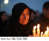 Elderly Woman Lights Candles at Dusk, Grieving With Soft Candlelight Around Her. symbolizing Memorials and Spiritual Gatherings. Стоковое AI-изображение, AI-художник Sergey Grishin / Фотобанк Лори