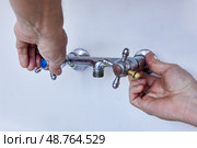 Two hands are loosening worn metal faucet with cross handles, spout is missing from central outlet, surface of fixture shows visible signs of use. Стоковое фото, фотограф Владимир Григорьев / Фотобанк Лори