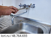 Person is tightening faucet spout to wall-mounted tap using adjustable wrench while standing over kitchen sink with visible metal drainer. Стоковое фото, фотограф Владимир Григорьев / Фотобанк Лори