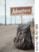 A worn backpack leaning against a vintage "Adventure" road sign. A white drawing symbolizing freedom. Стоковое AI-изображение, AI-художник Ярославский Максим / Фотобанк Лори