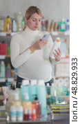 Thoughtful pregnant woman scanning bottle of sunscreen in personal care store using phone, checking ingredients to find safest option for her and future baby before making mobile payment. Стоковое видео, видеограф Яков Филимонов / Фотобанк Лори