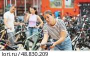 Interested young female cyclist choosing new bike for cycling trips in busy store, carefully picking comfortable bicycle saddle. Стоковое видео, видеограф Яков Филимонов / Фотобанк Лори