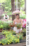 Young Spaniard woman in light white dress examining delicate brightly colored flowers of calibrachoa million bells in pots while selecting ornamental plants to decorate courtyard at garden store. Стоковое видео, видеограф Яков Филимонов / Фотобанк Лори