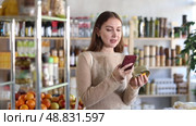 Young woman customer at shop scans QR code on tin cans of preserves using phone camera. Стоковое видео, видеограф Яков Филимонов / Фотобанк Лори