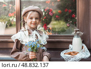 Vintage accessories and retro-style clothes. A small, beautiful girl with bows in her hair, in a beige dress and a beret outdoors with bagels and milk in a string bag. Стоковое фото, фотограф Photojuli / Фотобанк Лори