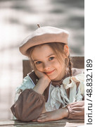 Vintage women's accessories and retro-style clothing. A small, beautiful girl with bows in her hair, in a beige dress and a beret outdoors. Стоковое фото, фотограф Photojuli / Фотобанк Лори