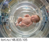 Новорожденный в искусственной утробе с контролем температуры, окруженный медицинским оборудованием. Стоковое AI-изображение, AI-художник Сергей Никифоров-Гордеев / Фотобанк Лори