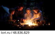 Family bonding around a campfire while toasting marshmallows on a cool evening in the woods. Стоковое AI-изображение, AI-художник Сергей Толмачёв / Фотобанк Лори