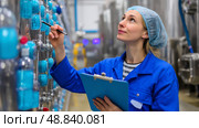 Technician monitors equipment in manufacturing facility while documenting data in a bustling industrial environment. Стоковое AI-изображение, AI-художник Сергей Толмачёв / Фотобанк Лори