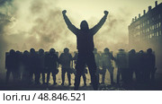 A hooded protestor stands defiantly with arms raised in front of a line of police officers holding shields. Стоковое AI-изображение, AI-художник Данила Большаков / Фотобанк Лори