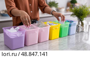 Organizing recyclable materials in colorful bins at a kitchen counter during daylight hours. Стоковое AI-изображение, AI-художник Сергей Толмачёв / Фотобанк Лори