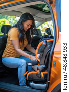 A woman in a yellow shirt and blue jeans is installing a car seat in the backseat of a vehicle. Стоковое AI-изображение, AI-художник Данила Большаков / Фотобанк Лори