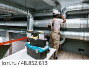 HVAC technician installing ductwork in a modern commercial space during daylight hours. Стоковое фото, фотограф Сергей Толмачёв / Фотобанк Лори