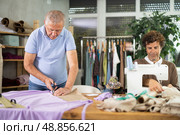 Man seamstress cuts fabric on cutting table, other master sew suit from cotton fabric. Стоковое фото, фотограф Яков Филимонов / Фотобанк Лори