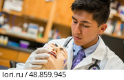 A medical student wearing a lab coat and stethoscope carefully practices suturing techniques on a mannequin. Стоковое AI-изображение, AI-художник Данила Большаков / Фотобанк Лори