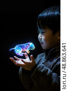 A young boy holds his hands out, mesmerized by a vibrant, holographic animal projection hovering between his palms. Стоковое AI-изображение, AI-художник Данила Большаков / Фотобанк Лори