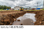 Construction site with heavy machinery creating a water-filled trench on a cloudy day. Стоковое AI-изображение, AI-художник Александр Калинин / Фотобанк Лори