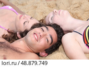 Three young people lying in the sand. Стоковое фото, агентство Ingram Publishing / Фотобанк Лори