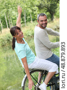 a couple doing bike in the country, the woman is doing airplane with her arms. Стоковое фото, агентство Ingram Publishing / Фотобанк Лори