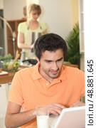 Man looking at his laptop while his wife prepares dinner. Стоковое фото, агентство Ingram Publishing / Фотобанк Лори