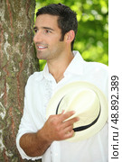 Man with straw hat leaning against tree. Стоковое фото, агентство Ingram Publishing / Фотобанк Лори