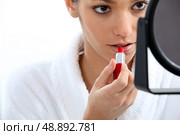 Woman applying lipstick in front of mirror. Стоковое фото, агентство Ingram Publishing / Фотобанк Лори