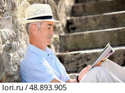 Senior man reading a magazine on some old stone steps. Стоковое фото, агентство Ingram Publishing / Фотобанк Лори