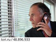 Senior businessman looking through blinds whilst making call. Стоковое фото, агентство Ingram Publishing / Фотобанк Лори