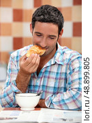 Smiling man eating croissant for breakfast with a magazine. Стоковое фото, агентство Ingram Publishing / Фотобанк Лори