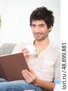 young man reading a book and drinking coffee on a couch. Стоковое фото, агентство Ingram Publishing / Фотобанк Лори