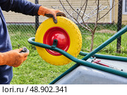 Checking central bore and positioning axle rod to ensure correct fit of solid tire for upcoming mounting on metal frame of garden wheelbarrow. Стоковое фото, фотограф Владимир Григорьев / Фотобанк Лори